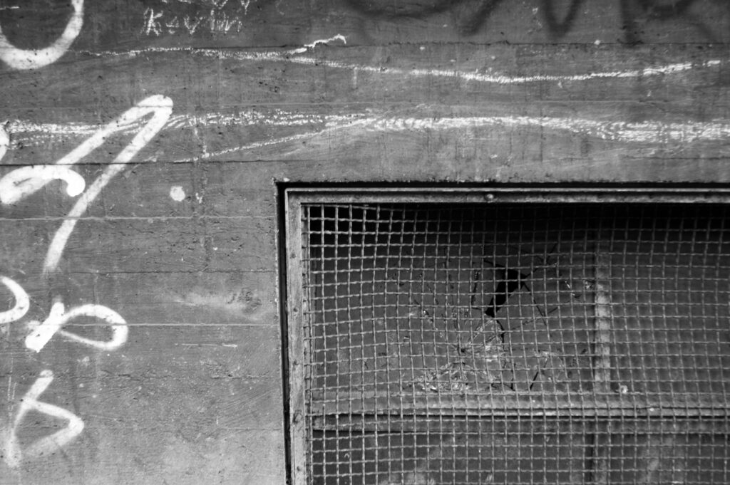 Ein Gitter in einer Betonwand, dahinter zerbrochenes Glas. 